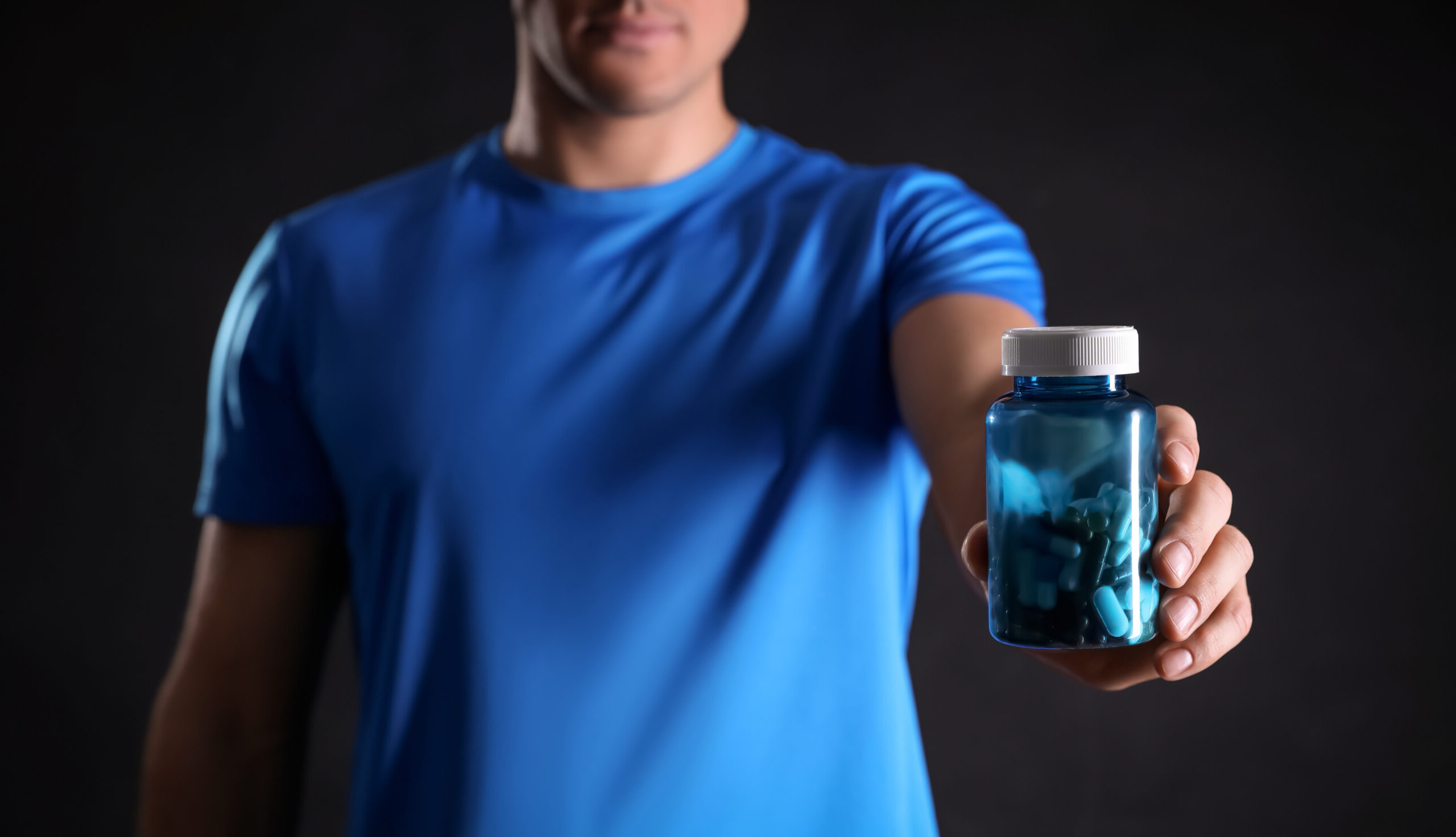 Man with bottle of pills on black background, closeup. Doping concept